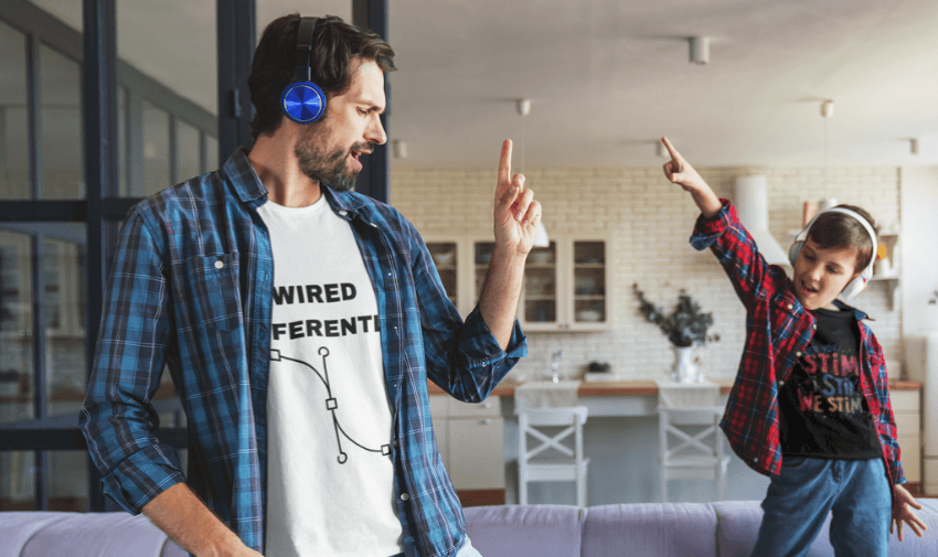 A man and a child wearing headphones and plaid shirts are dancing together in a living room. The man has a white shirt with "Wired Different" on it, while the child wears a black shirt. They are both raising one hand and smiling.