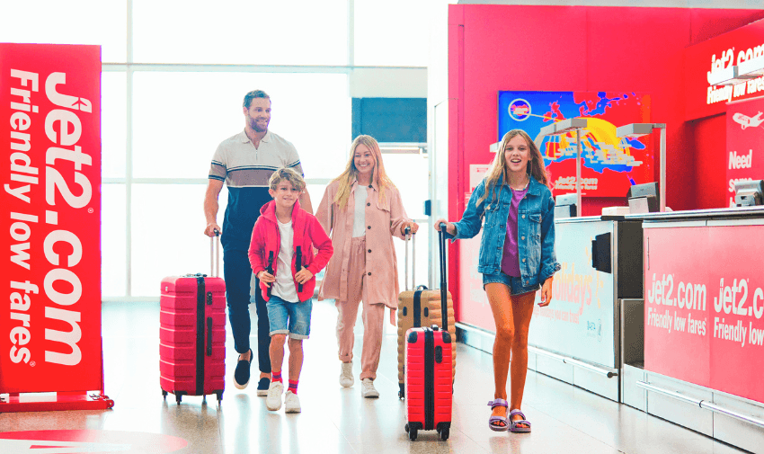 main image - A family of four walking through an airport with bright red Jet2.com signage, carrying colourful luggage and smiling. Showcasing Purpl's disabled travel discounts with Jet2 Holidays, promoting affordable and accessible travel options for families.