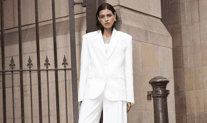 A woman with dark hair is wearing a white suit with an oversized jacket.