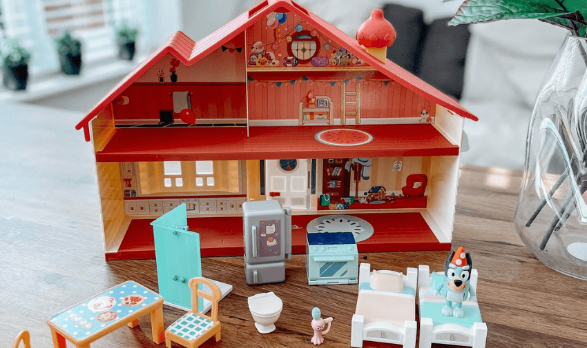 A colourful dollhouse playset with furniture and Bluey-themed characters displayed on a wooden table in a bright living room. Highlights Toy Discounts for Disabled Children and Shopping Discounts for Disabled Families.