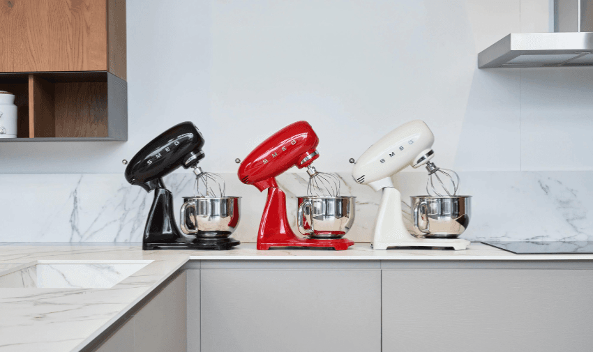 Three Smeg food processors in different colours - black, red and cream lined up in a row on a kitchen surface