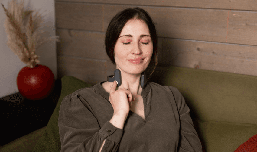 A woman sitting on a sofa with her eyes closed, using a Pulsetto relaxation device on her neck for stress relief. Highlighting Purpl's exclusive disabled discounts for wellness and relaxation aids in the UK.