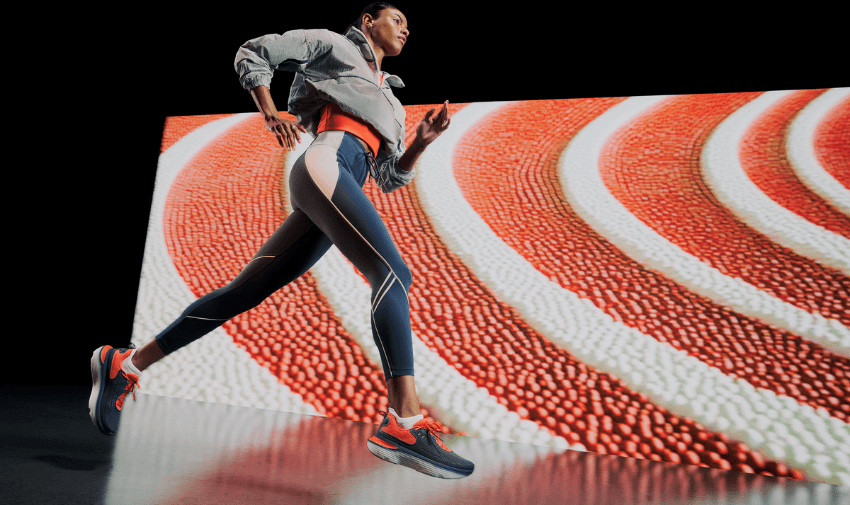 A female athlete in dynamic motion wearing Under Armour activewear, running in front of a bold, red and white graphic backdrop. Ideal for mobility discounts and offers on high-performance sports gear for disabled people.