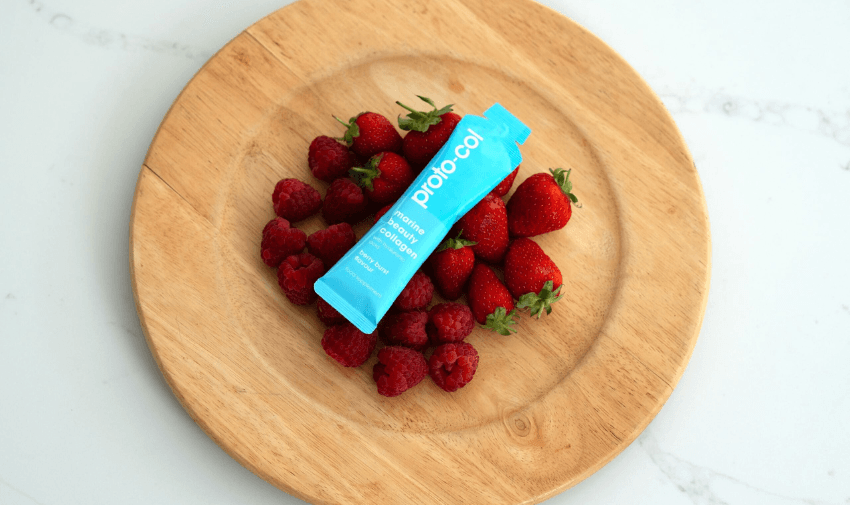 A wooden plate with fresh strawberries and raspberries, featuring a blue sachet of Proto-col marine collagen supplement. The collagen sachet is placed at the center of the fruits, highlighting its berry blend flavour. A refreshing and natural supplement choice. Keywords: Collagen Supplements UK, Marine Collagen Beauty, Skin and Hair Health.