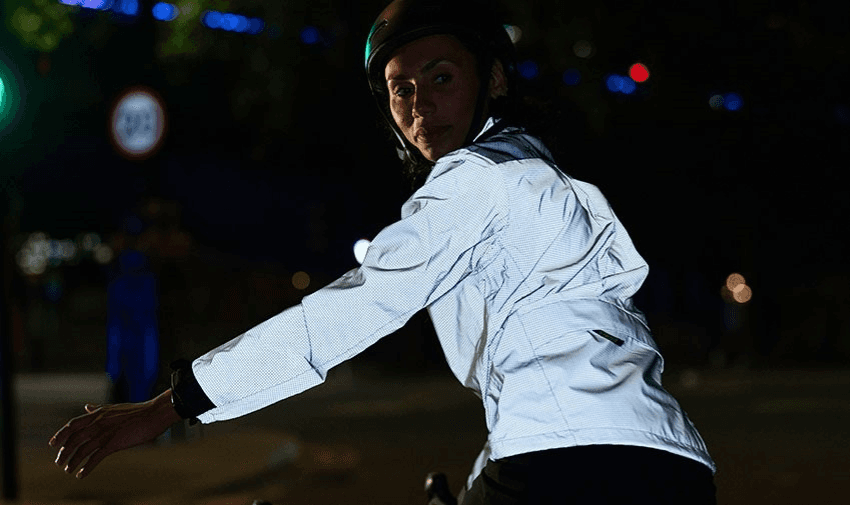 A cyclist wearing a reflective Proviz jacket while signalling at night, enhancing visibility and safety on the road. Highlighting Purpl's exclusive disabled discounts for adaptive and high-visibility cycling gear in the UK.