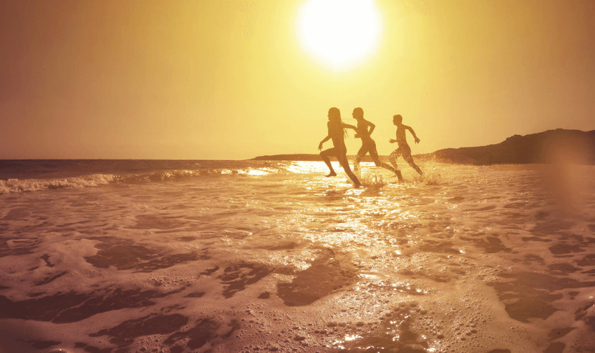 Three people running joyfully in the shallow waves at sunset, with a glowing golden sky reflecting on the ocean. Perfect for EasyJet Holidays travel inspiration.