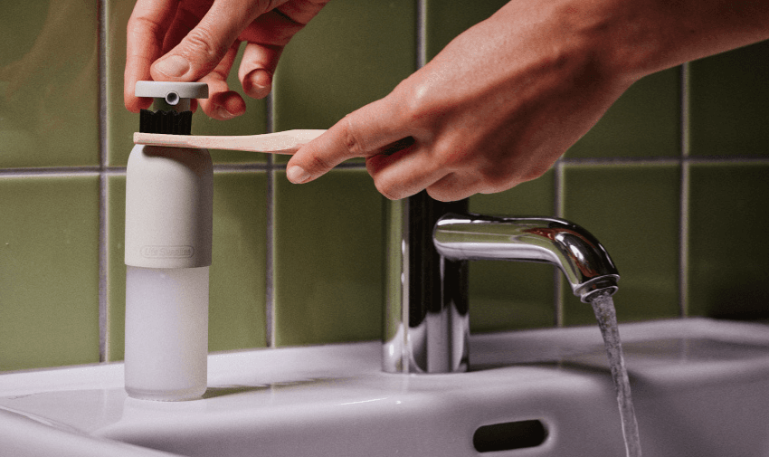 A refillable toothbrush dispenser being used with a wooden toothbrush on a bathroom sink, symbolising eco-friendly oral care. Highlighting Purpl's exclusive disabled discounts for sustainable and adaptive personal care products in the UK.