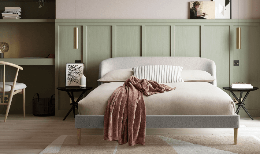 A modern bedroom features a minimalist design with a soft beige bed, a striped pillow, and a textured pink throw blanket. Two round black side tables hold small decor pieces, and pendant lights hang overhead. A light green panelled wall adds texture.