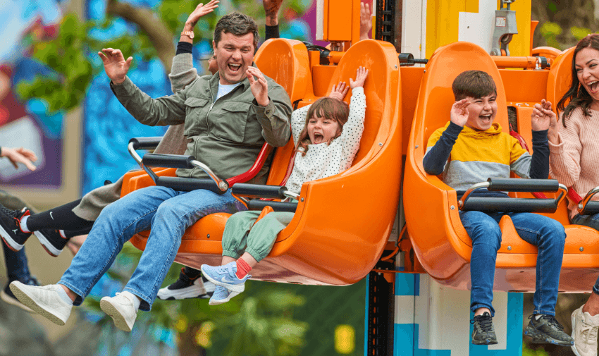 A family enjoying a thrilling drop tower ride, laughing and raising their hands in excitement while seated in bright orange seats.