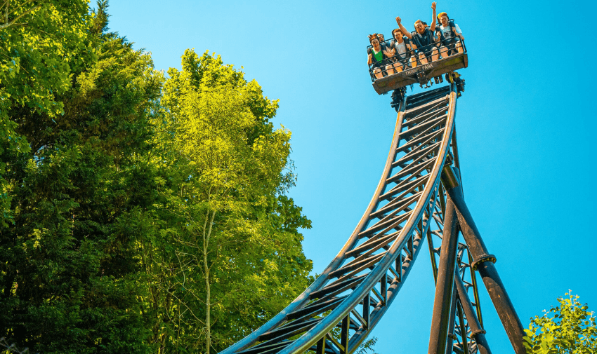 A group of thrill-seekers riding a steep roller coaster drop at Thorpe Park, surrounded by lush trees and a bright blue sky. Highlights Theme Park Discounts for Disabled Visitors and Free Carer Tickets UK.