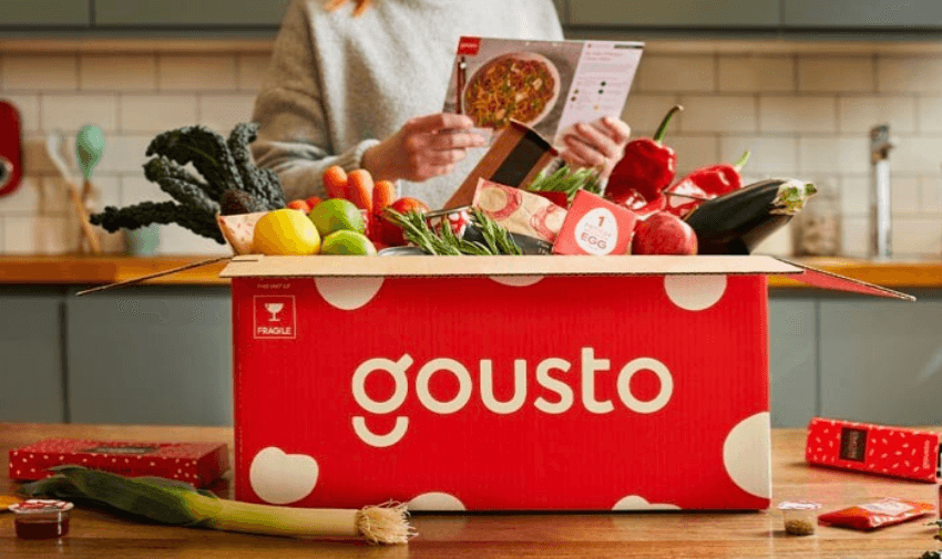 A red Gousto recipe box filled with fresh vegetables, fruits, and herbs on a kitchen counter, promoting easy meal kits. Purpl's disabled discounts make healthy eating and accessible cooking affordable for disabled individuals in the UK.