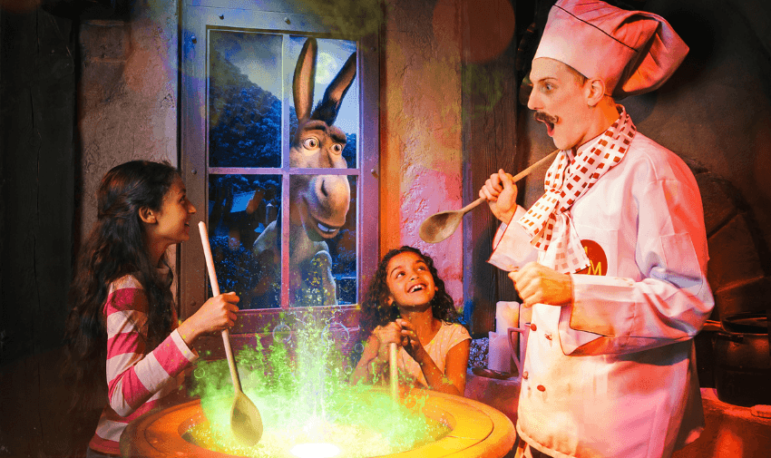 Shrek Adventure London interactive experience with children cooking alongside Shrek characters, featuring vibrant green magic effects.