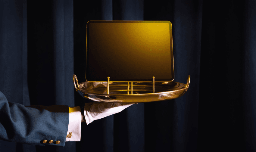 an arm dressed in a suit sleeve is holding a tray out with a yellow gold tablet on a gold stand