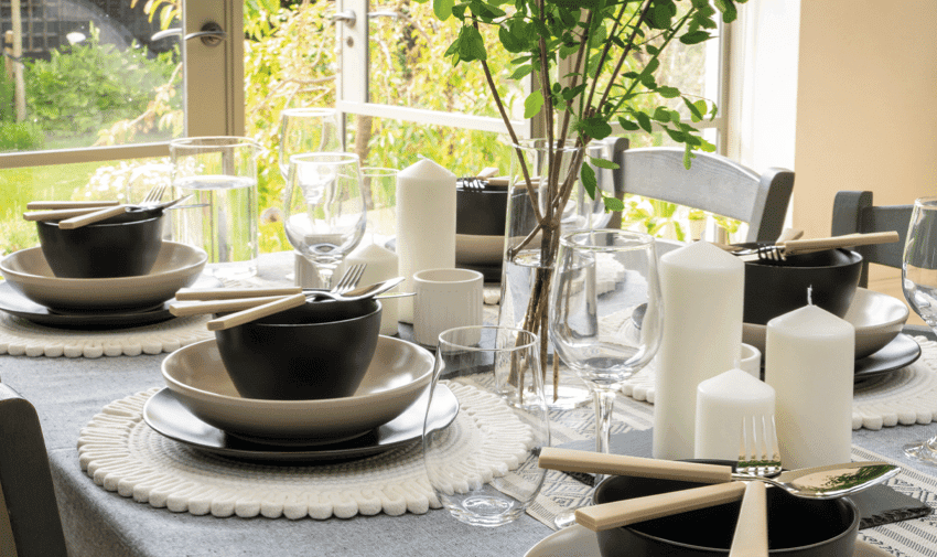 A dining table set with black and white dinnerware, including bowls, plates, and glasses. White candles and simple floral arrangements are placed in the centre.