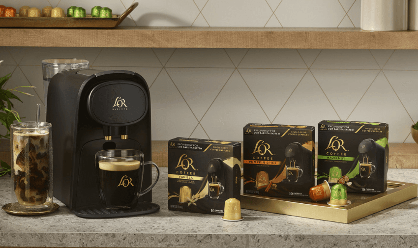 A coffee station featuring an espresso machine with a L’OR coffee cup filled with espresso. Nearby, there are three boxes of L’OR coffee pods in different colours and flavours, and an iced coffee with milk and ice on a counter with a greenery in the background.