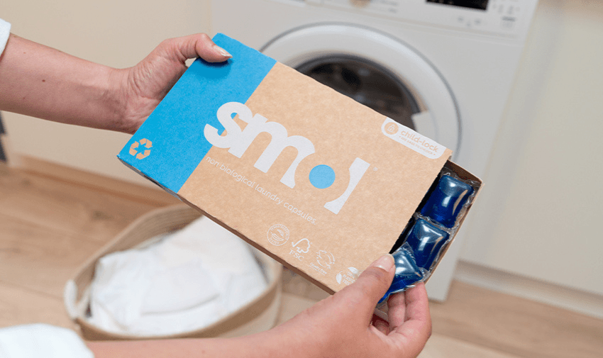 packet of smol non-bio laundry capsules being held out in front of a washing machine