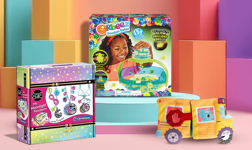 The image shows three colourful children's toy kits against a vibrant, geometric background. The toys include an art and craft jewellery set, an Orbeez Sensation Station, and a toy vehicle made from soft materials.