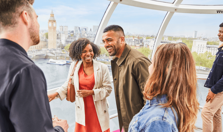 Group of people laughing inside the London Eye pod with a view of Big Ben and the River Thames in the background, showcasing a fun day out at London's iconic attraction.