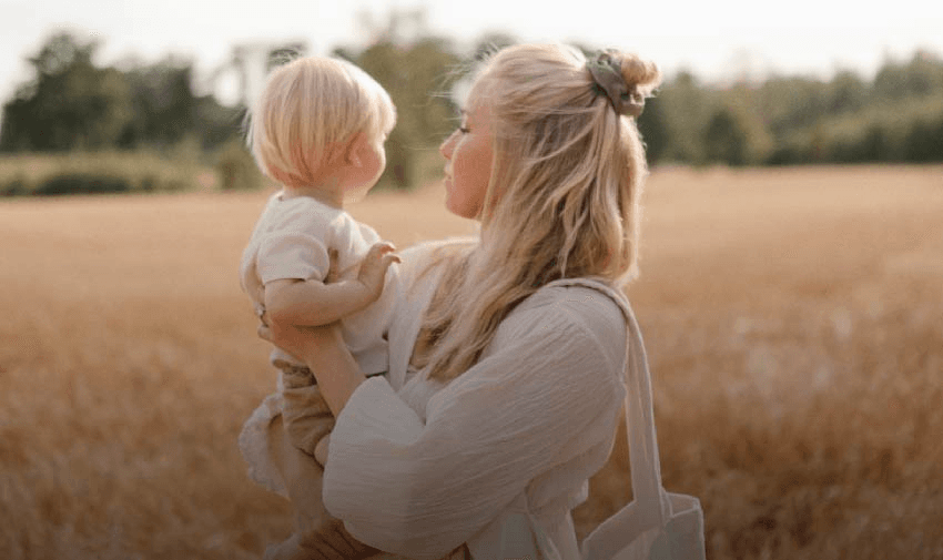 A mother holding her toddler in a golden wheat field, both gazing into the distance. Highlights Shopping Discounts for Disabled Parents and Baby Products Discounts.