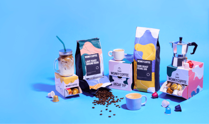 A colourful coffee display featuring "Wonky Coffee" products, including light roast, dark roast, and decaf options, surrounded by coffee beans, pods, a moka pot, and mugs of coffee, set against a bright blue background.