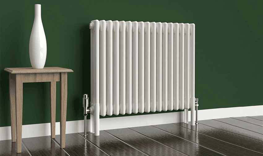 3 Column Horizontal Radiator in a white finish. Including matching column radiator feet with Angled Chrome Thermostatic Valves set against a dark green wall