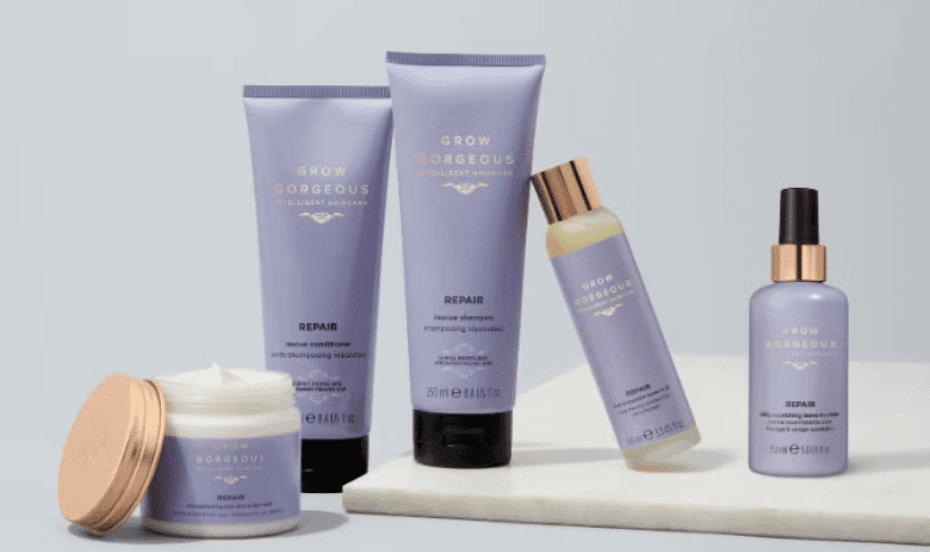 Image displays a collection of hair care products from the brand "Grow Gorgeous Repair." There is a jar of masque, two tubes of shampoo and conditioner, and two spray bottles, all in purple packaging with gold accents, arranged on a light-coloured surface.