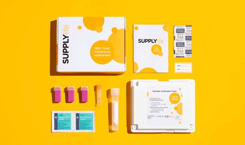 Image shows a food intolerance assessment kit from SupplyLife against a bright yellow background. The kit includes a box labeled "SupplyLife 200+ Food Intolerance Assessment," various sample collection tools, instruction booklets, adhesive labels, and alcohol wipes.