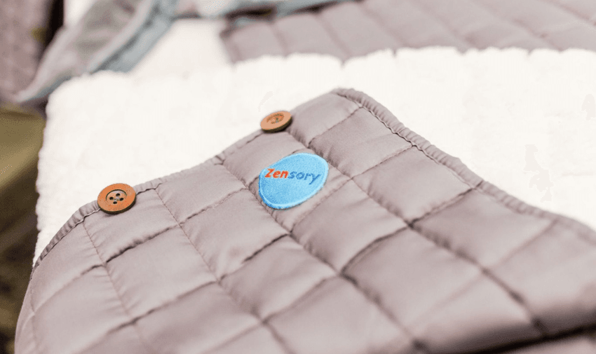 Close-up of a Zensory weighted blanket with a stitched logo and button details, showing its soft and quilted fabric.