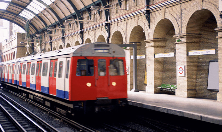 A classic red and white London Underground train arriving at the historic Notting Hill Gate station with arched brickwork. Showcasing TrainPal and Purpl's disabled travel discounts, promoting accessible and affordable public transport options across the UK.