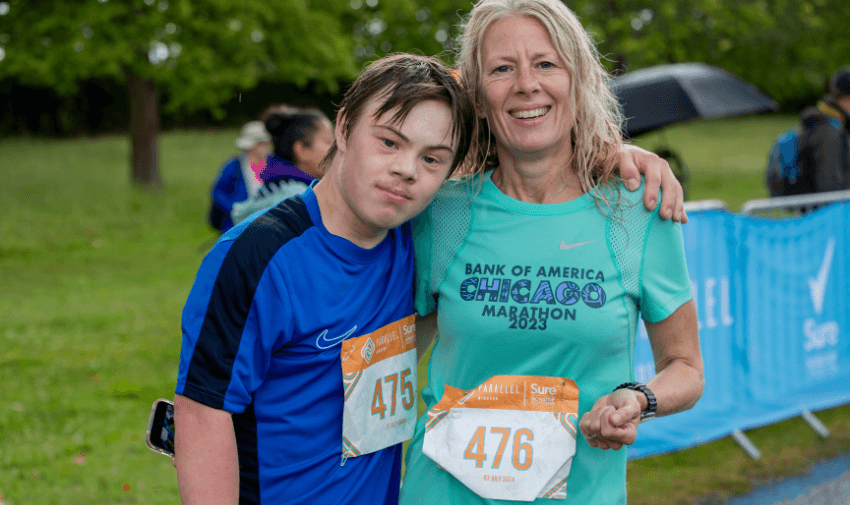 A young man with Down syndrome and a woman smiling at the finish line of the Parallel Windsor event, both wearing race bibs. Highlighting Purpl's exclusive disabled discounts for inclusive sporting events and activities in the UK.