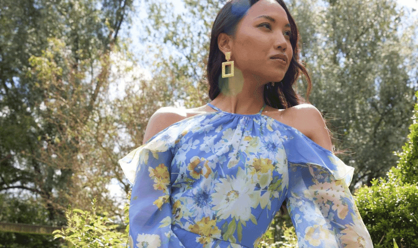 A women is wearing a blue floral halter-neck dress from Oasis, she is standing outside in a garden.