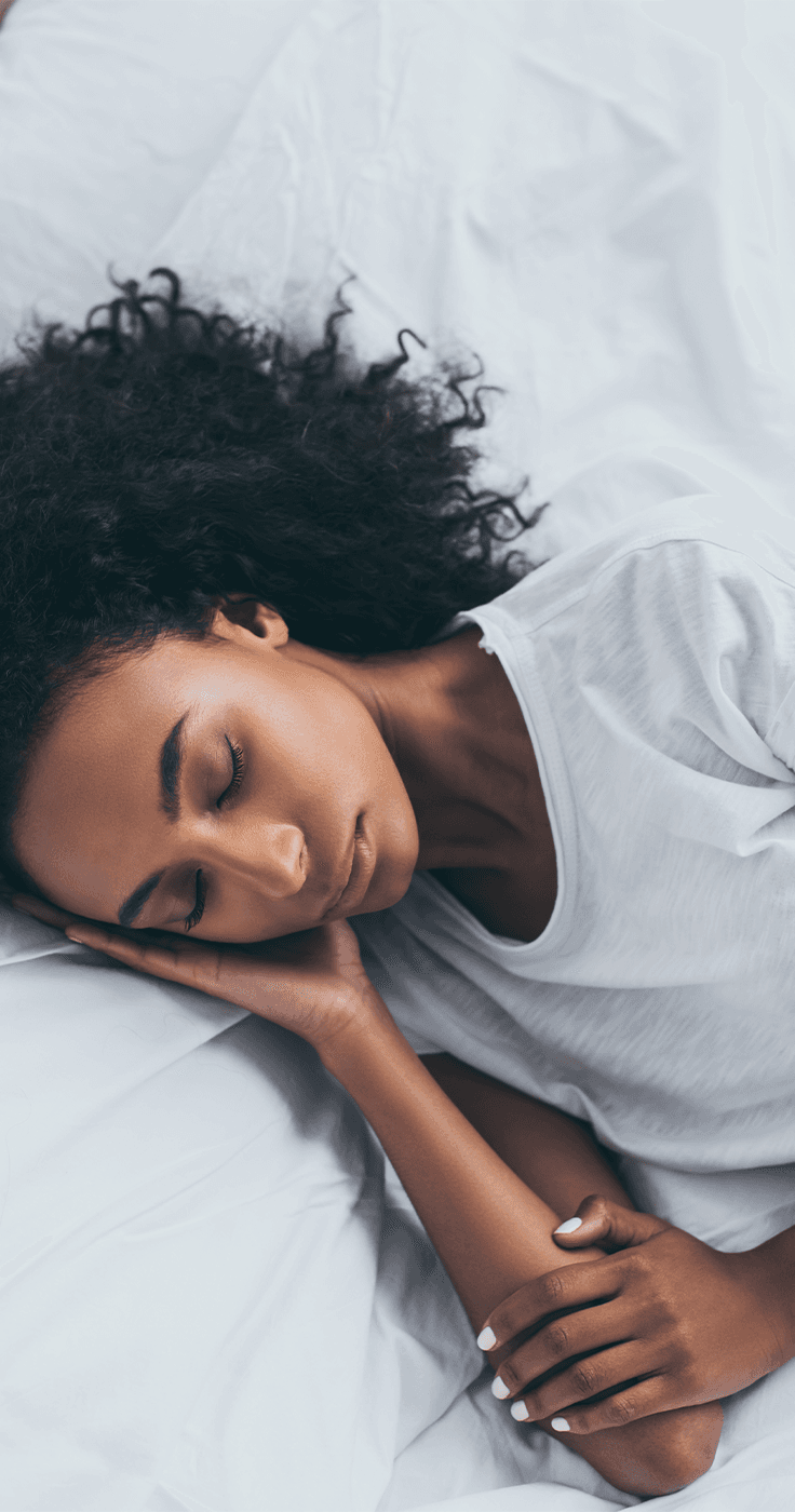 A person stretches and smiles while lying in bed under a white blanket. 