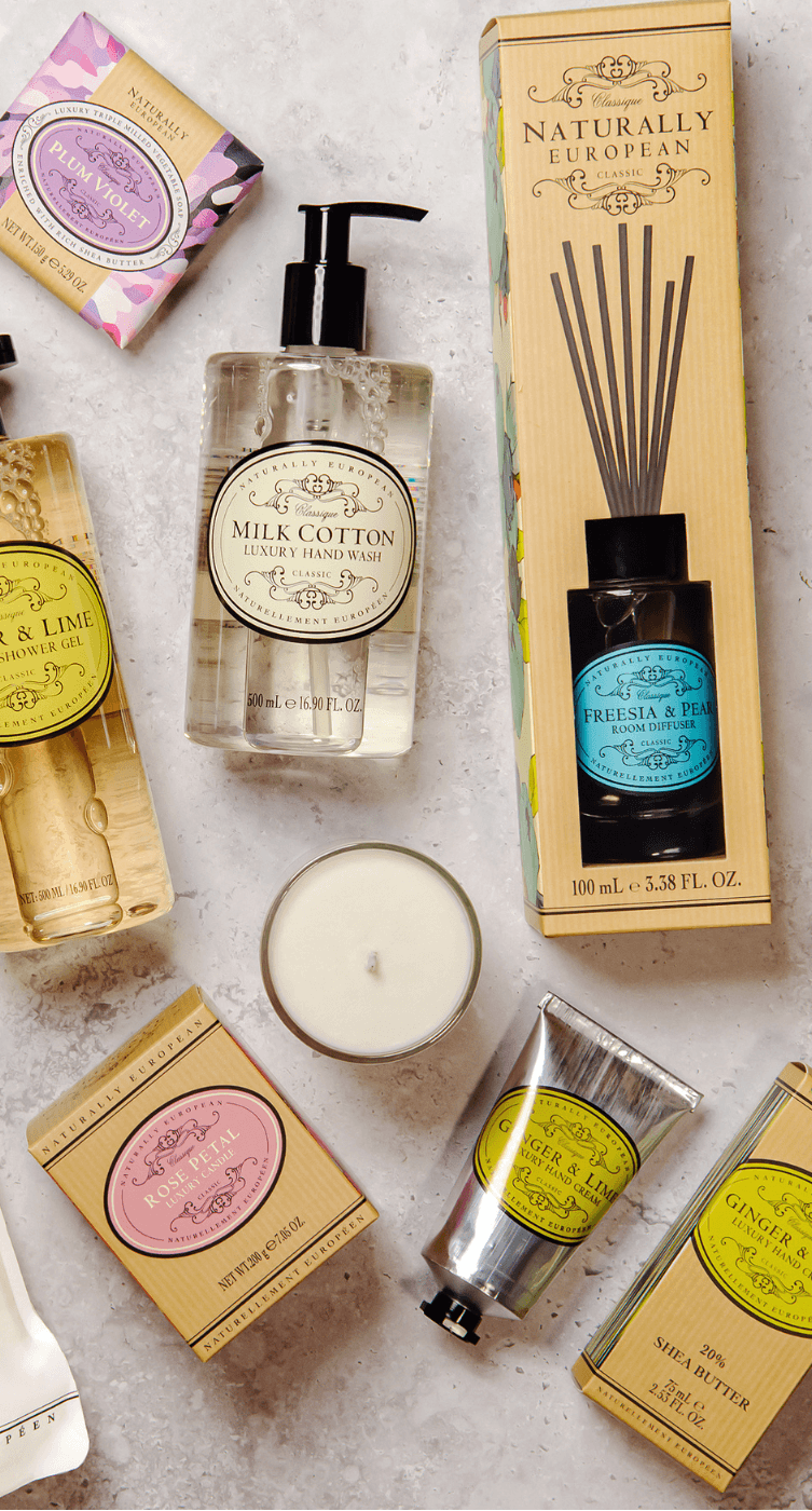 A flat lay of various Somerset Toiletry Co products arranged on a neutral background. Items include hand washes, lotions, a candle, a diffuser, and scented oils. 