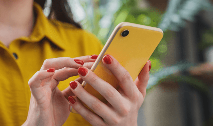 A person holding a yellow smartphone with red nail polish. 