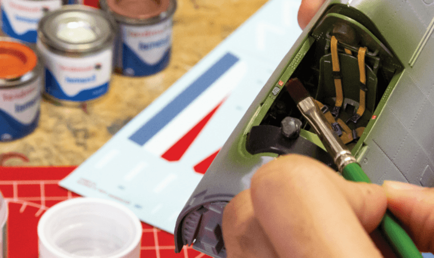 a person painting a model airplane with Humbrol paints in the background