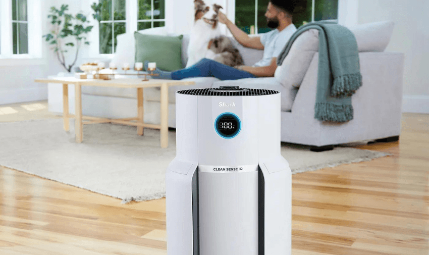 Shows a Shark NeverChange5 Air Purifier MAX HP300UK in a lounge with a man sitting on a sofa in the background