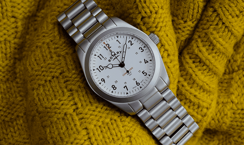 A stainless steel rotary watch resting on a soft, yellow blanket.