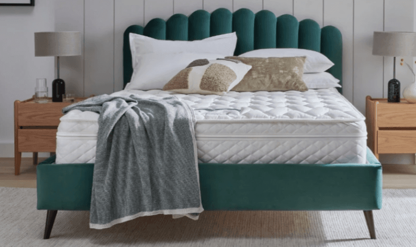 A luxurious green velvet bed with a plush headboard, dressed with a white quilted mattress, stylish pillows, and a soft grey throw. The bedside tables and lamps complete the cosy look. Mobility Discounts and Offers, Disabled Home Furnishing Deals UK.