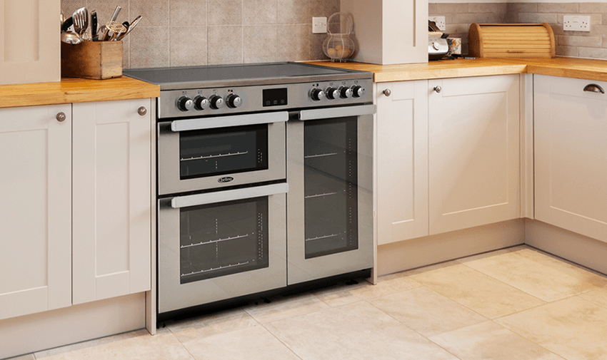  A modern kitchen features a freestanding stainless steel double oven. There are wooden countertops with utensils in containers and a white bread box placed on top. The cabinets are white and the floor is covered with beige tiles.