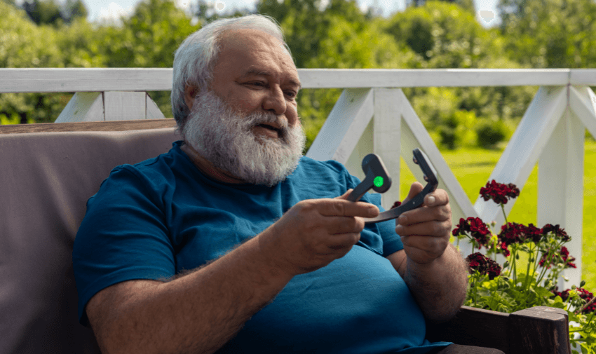 A man sitting outside on a sunny day, smiling while holding a Pulsetto relaxation device, designed to support stress and anxiety relief. Showcasing Purpl's disabled discounts for innovative health and wellbeing products in the UK.