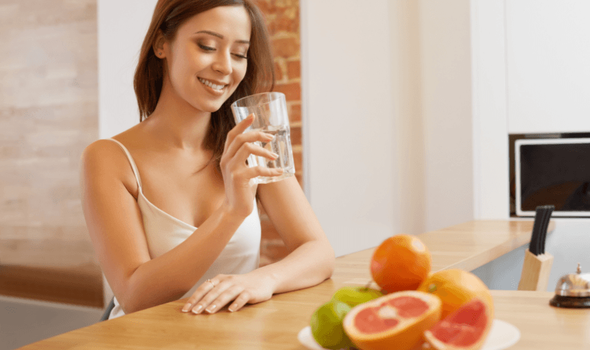 A woman enjoying a glass of water, seated near a plate of fresh fruits, symbolising a healthy lifestyle with Simply Sensitivity Checks. Promoting Purpl's affordable health testing discounts for disabled individuals seeking personalised wellbeing solutions in the UK.