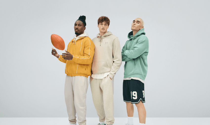 Three men modelling Under Armour casual sportswear, including hoodies, joggers, and shorts, standing confidently in a studio setting. Perfect for showcasing shopping discounts for disabled people on inclusive and comfortable athletic clothing.