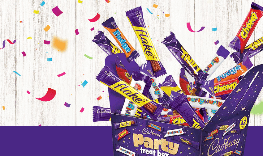 An open box labeled "Cadbury Party Treat Box" is filled with various Cadbury chocolate bars including Flake, Fudge, Chomp, and Twirl. Colourful confetti is scattered around, celebrating the assortment of sweets. The background is a mix of white, wood-like texture, and purple.