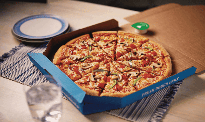 Domino's Veggie Supreme pizza in a Domino’s delivery blue cardboard box open on a dining table.