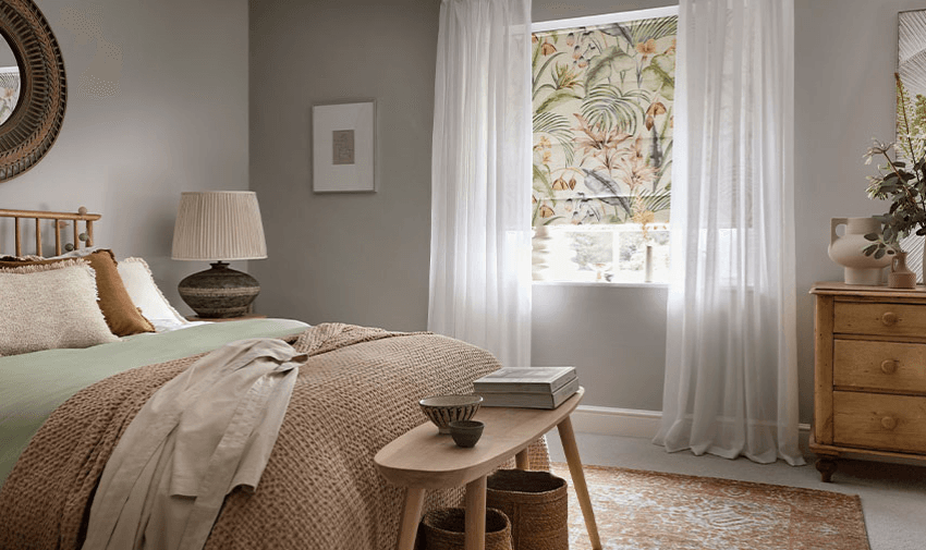 Cosy bedroom featuring a tropical floral blackout roller blind and soft white curtains. Great for improved sleep and sensory comfort. Ideal for mobility discounts and home adaptation offers for disabled individuals in the UK.