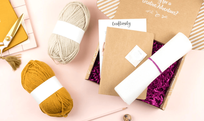 An open Craftiosity kit featuring yarn, crafting materials, and a notebook displayed on a pastel workspace. Includes shopping discounts for disabled people and creative hobby discounts.