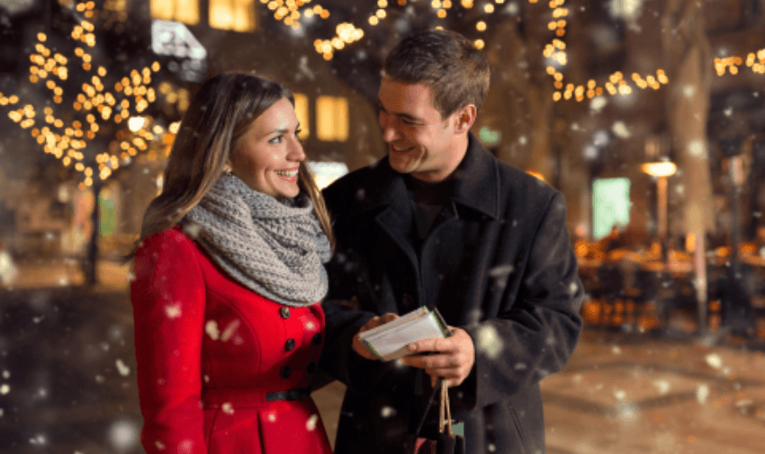 A festive couple enjoying a magical winter evening gift exchange amidst sparkling holiday lights.