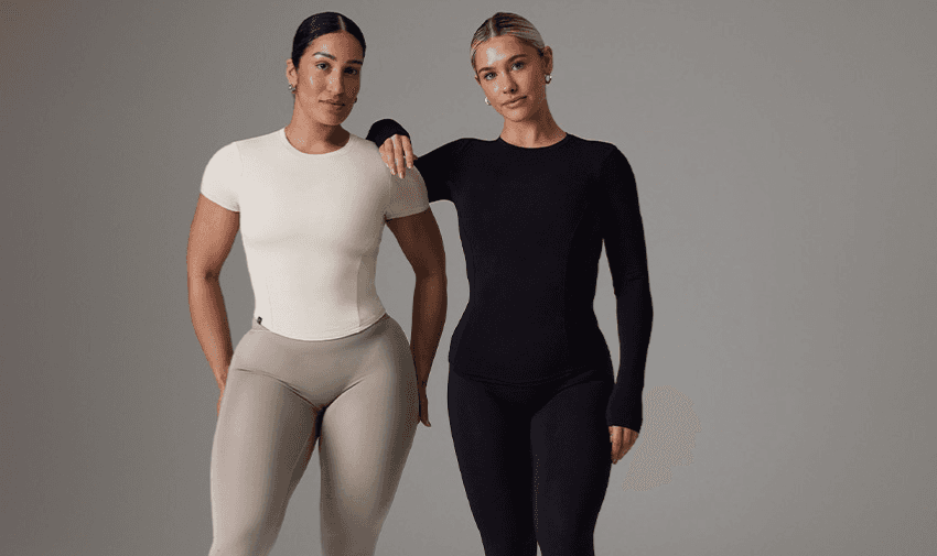 Two women standing side by side, both wearing Oner Active form-fitting workout clothes. The woman on the left is in a beige top and light brown leggings, while the woman on the right is in a black long-sleeve top and black leggings. They stand against a plain grey background.