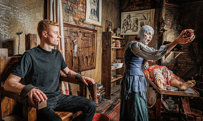 A torturous medieval scene at the London Dungeon with an actor and props, featuring a visitor tied to a chair in a dramatic performance.