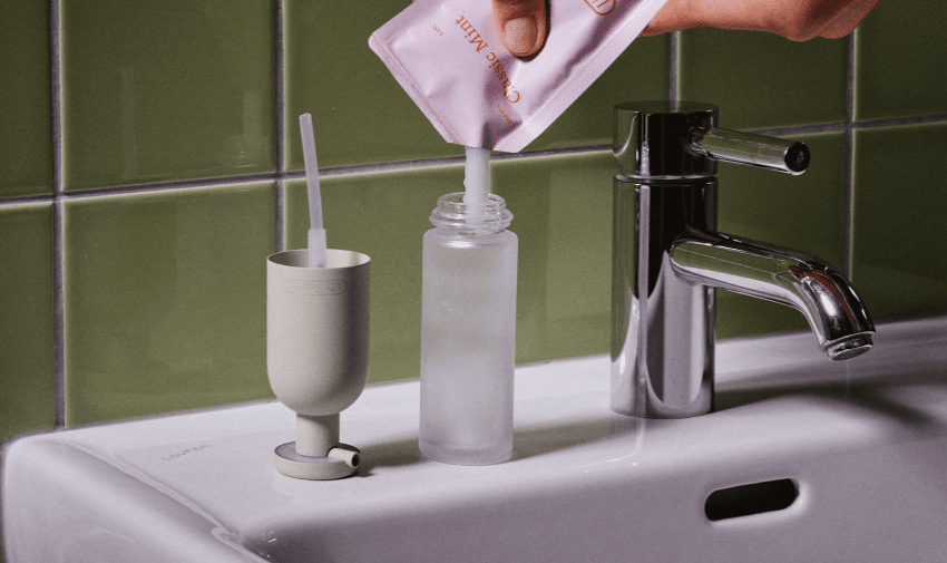 A reusable dispenser being filled with toothpaste from a refill pack on a bathroom sink, promoting zero-waste living. Showcasing Purpl's disabled discounts for sustainable personal care solutions, making eco-friendly products accessible in the UK.